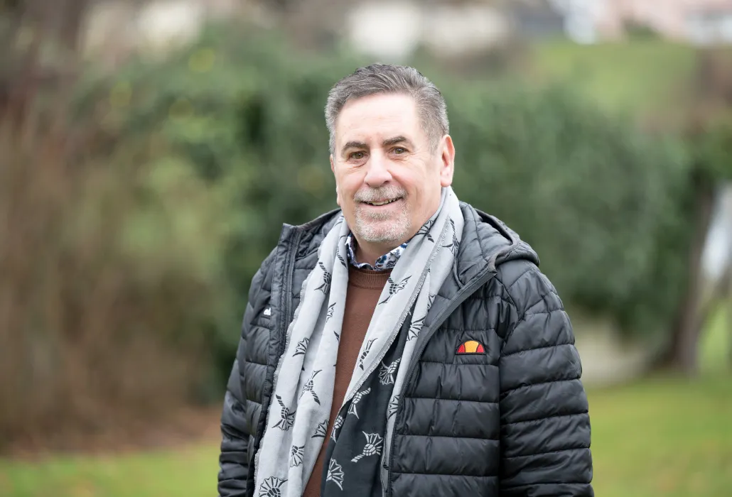 Hans-Peter Urech steht draussen und lächelt in die Kamera, im Hintergrund ist unscharf ein Gebüsch zu sehen.