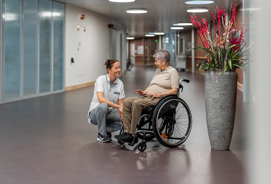 Mitarbeiterin mit Patientin im Rollstuhl