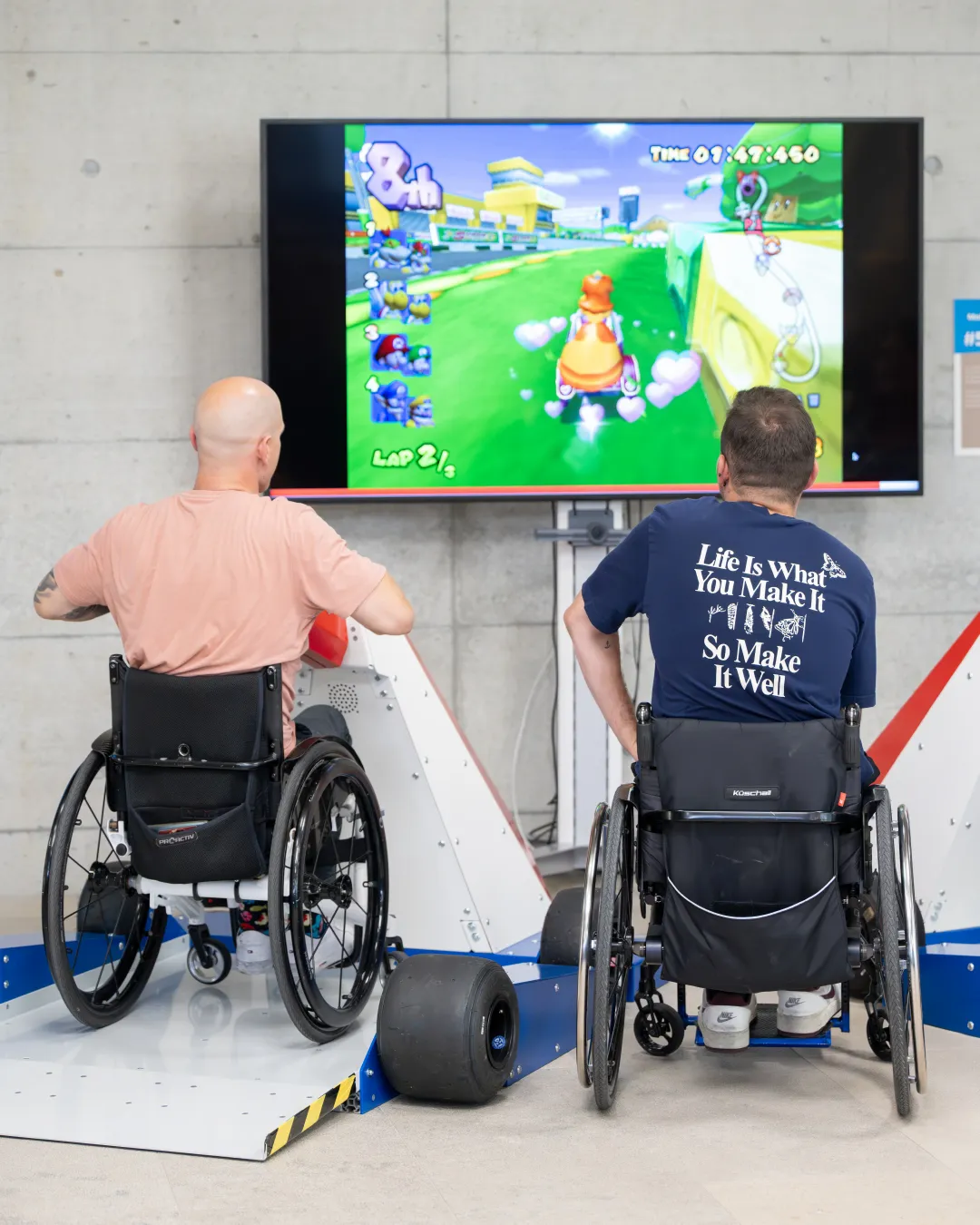 Zwei Personen spielen im Rollstuhl MarioKart. 