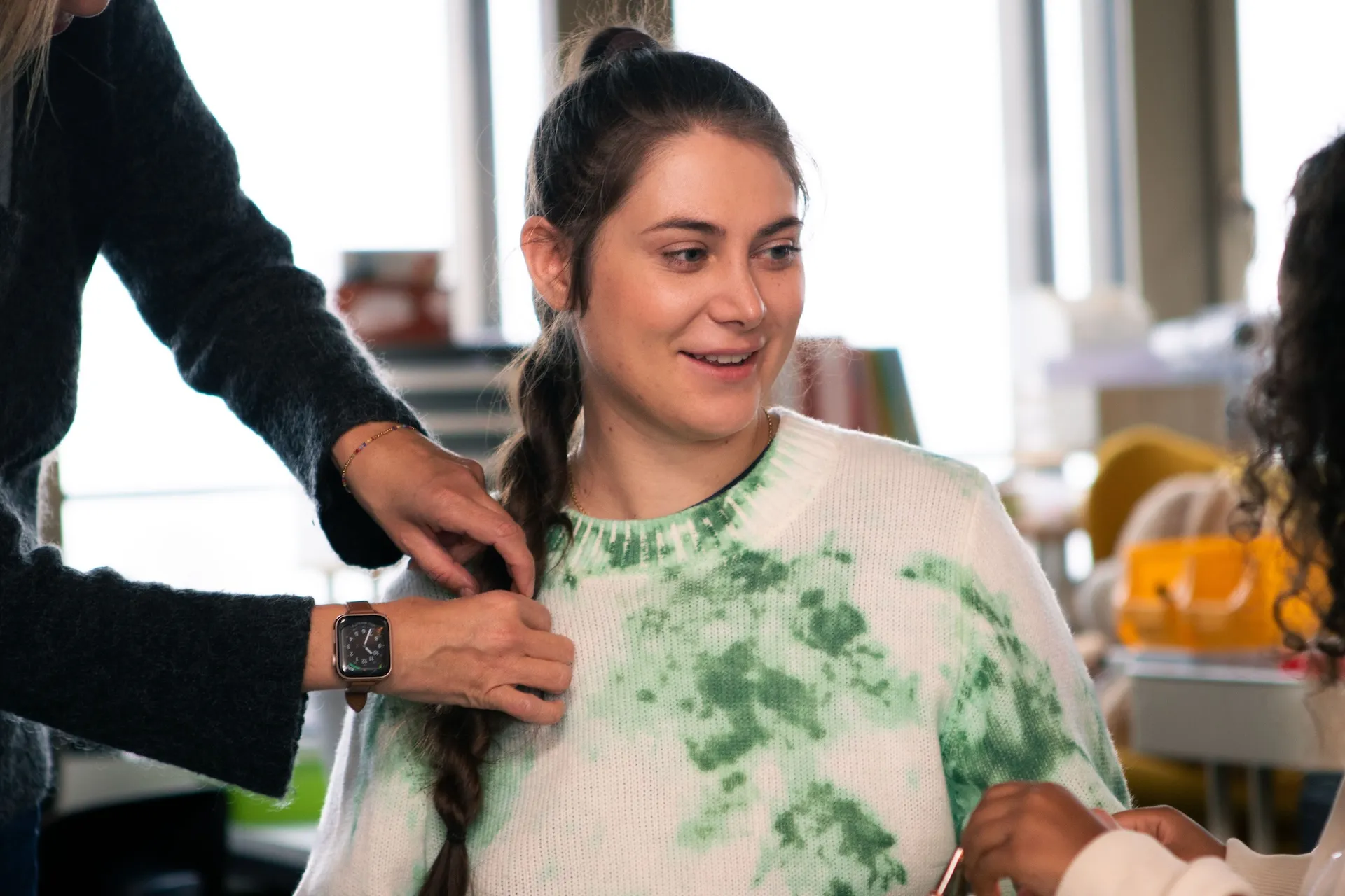 Chiara Schlatter blickt zu einer Schülerin, die rechts im Bild ein klein wenig zu sehen ist, während ihr die Stylistin den Zopf schön herrichtet.