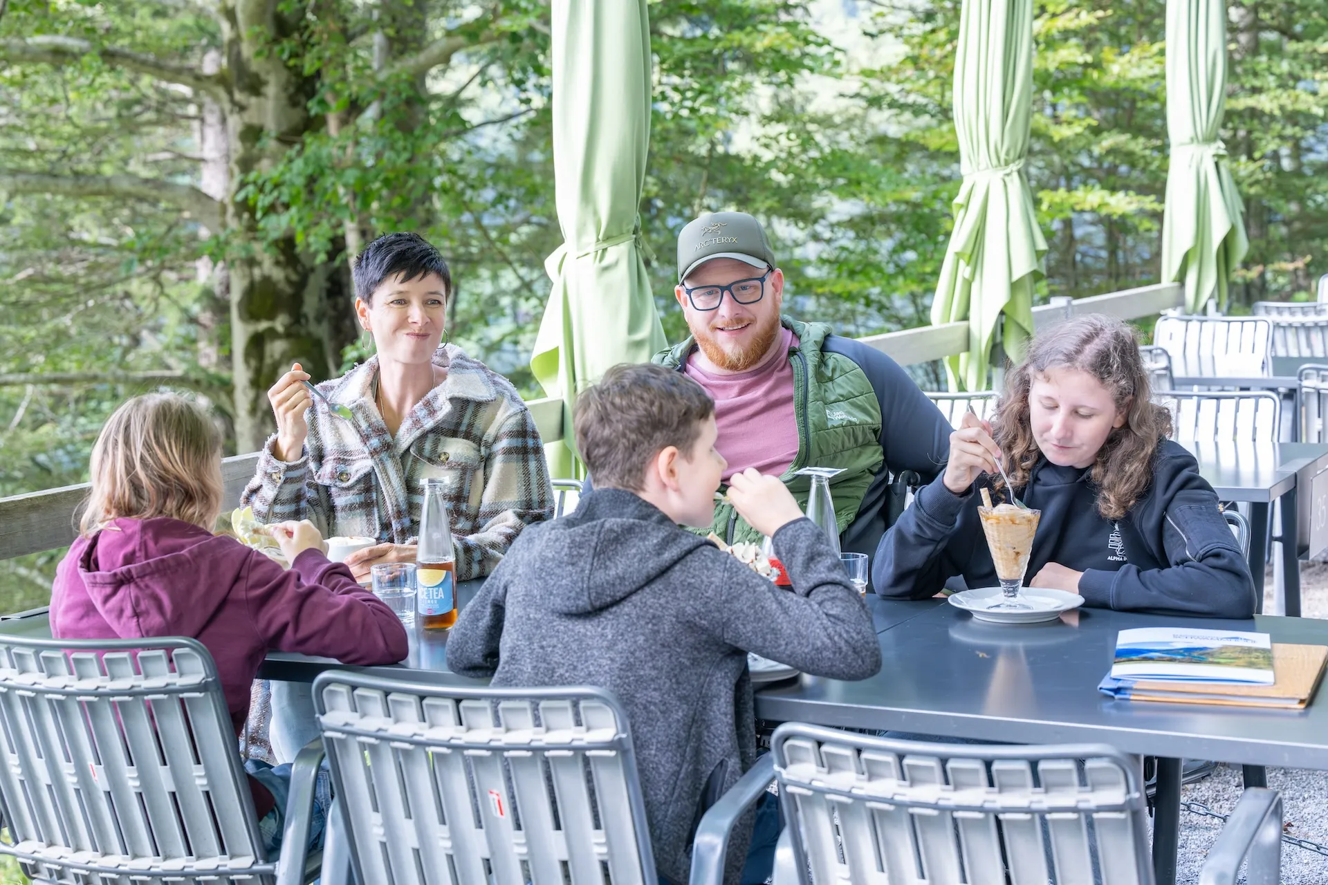 Heiri mit seiner Familie auf der Terrasse einer Gaststätte draussen in der Natur am Tisch.