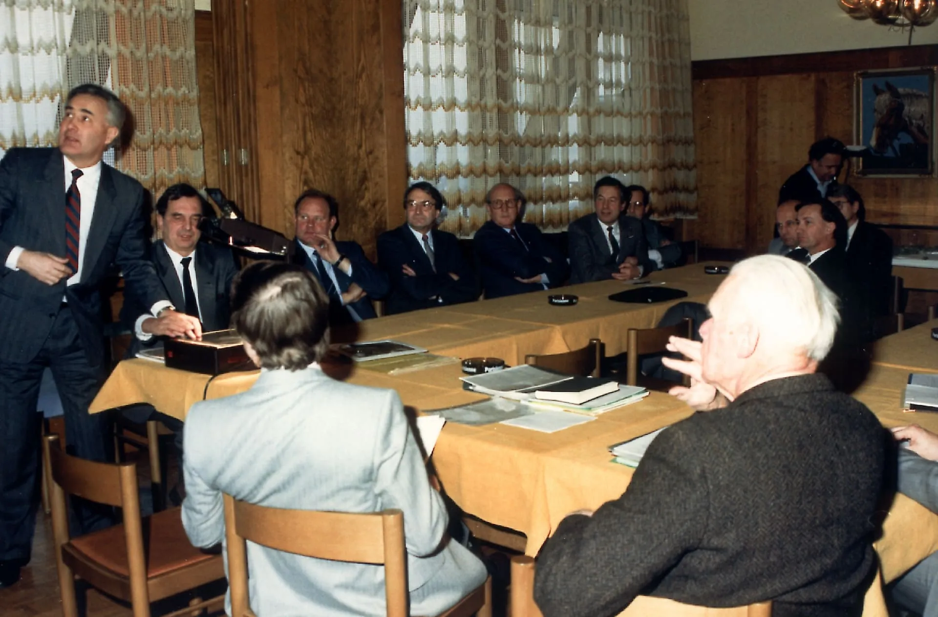 Guido A. Zäch steht ganz links im Bild in einem Raum, in dem der Gemeinderat Nottwil Tagt. Die Gemeinderatsmitglieder sitzen an einem U-Förmigen Konferenz-Tisch und blicken zu Zäch, der ihnen etwas präsentiert.