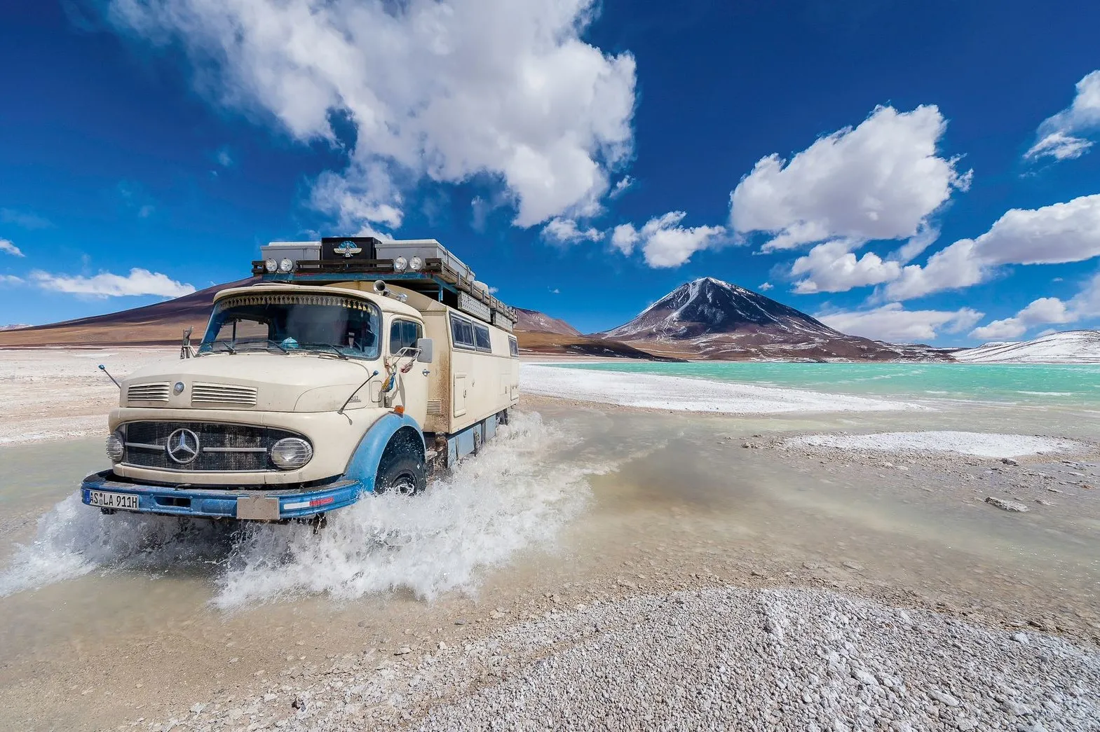 Explora - Freiheit auf 4 Rädern: Vollbepacktes Fahrzeug fährt durchs Wasser in einer atemberaubenden Landschaft.